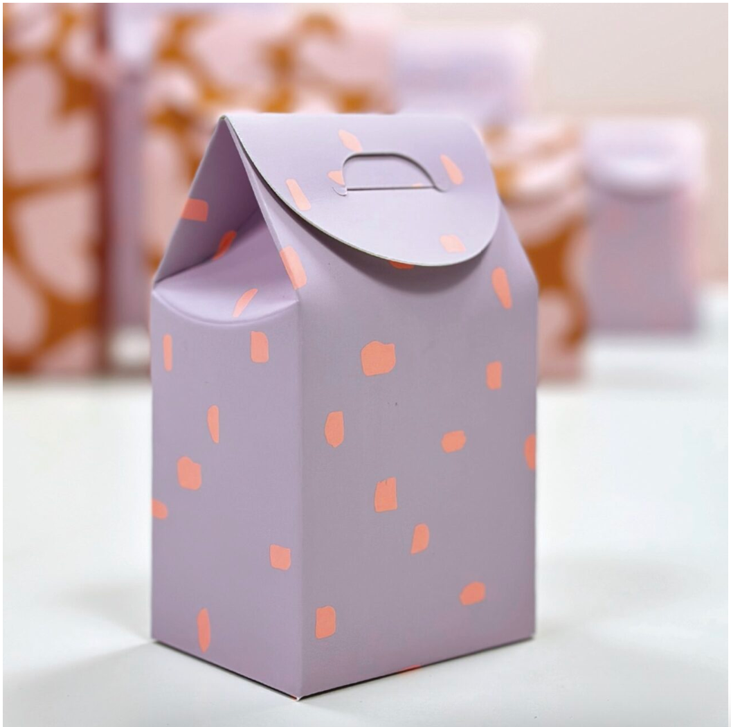 Geschenkbox in Rot, Lila und Neon steht im Vordergrund auf hellem Untergrund. Im Hintergrund sind unscharf weitere ähnliche Geschenkboxen zu sehen, die eine stimmungsvolle Verpackungsszene erzeugen.