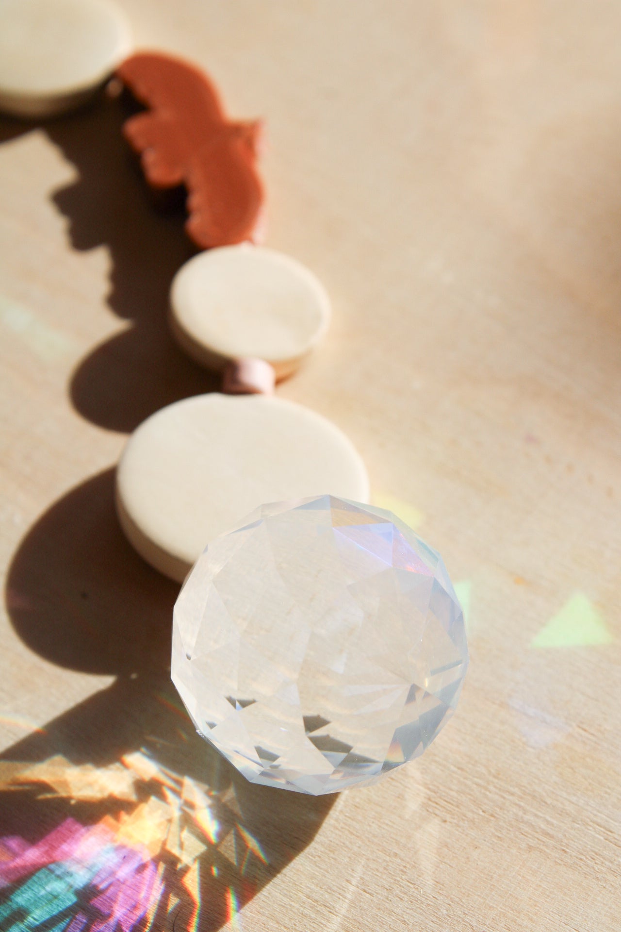 Suncatcher mit einer großen Kristallkugel, Holzperlen, Keramikperlen und 3D-Druck Perle in Form eines Vogels in einem warmen braun fotografiert auf hellem Holz.