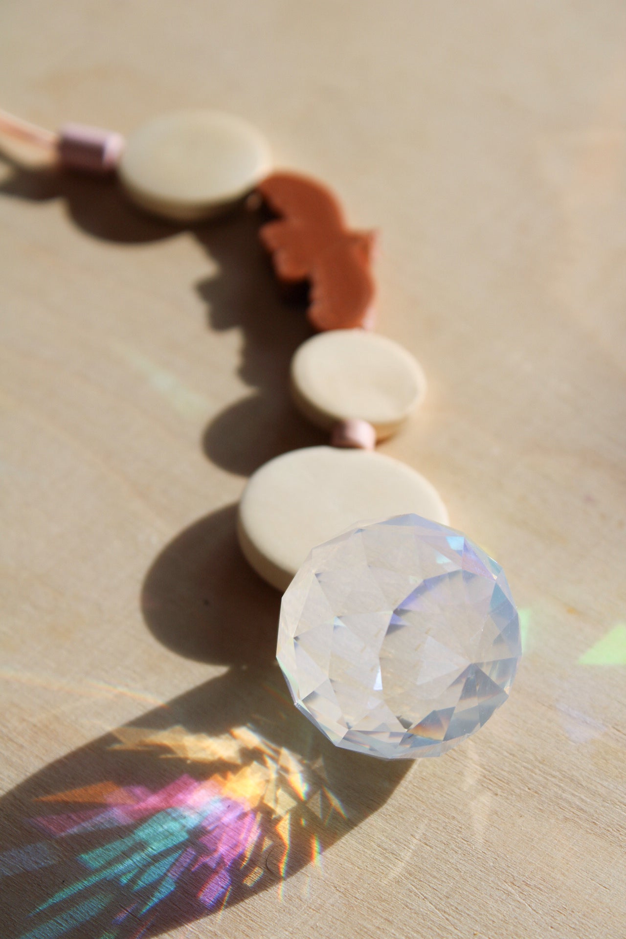 Suncatcher mit einer großen Kristallkugel, Holzperlen, Keramikperlen und 3D-Druck Perle in Form eines Vogels in einem warmen braun fotografiert auf hellem Holz.