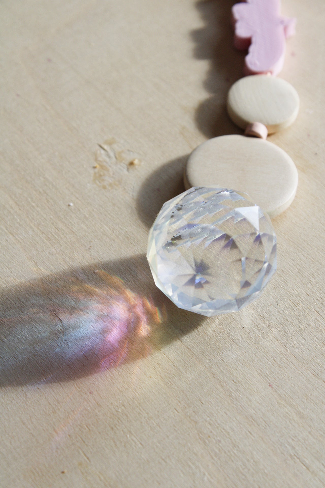Suncatcher mit einer großen Kristallkugel, Holzperlen, Keramikperlen und 3D-Druck Perle in Form eines Vogels in einem zarten rosa fotografiert auf hellem Holz.