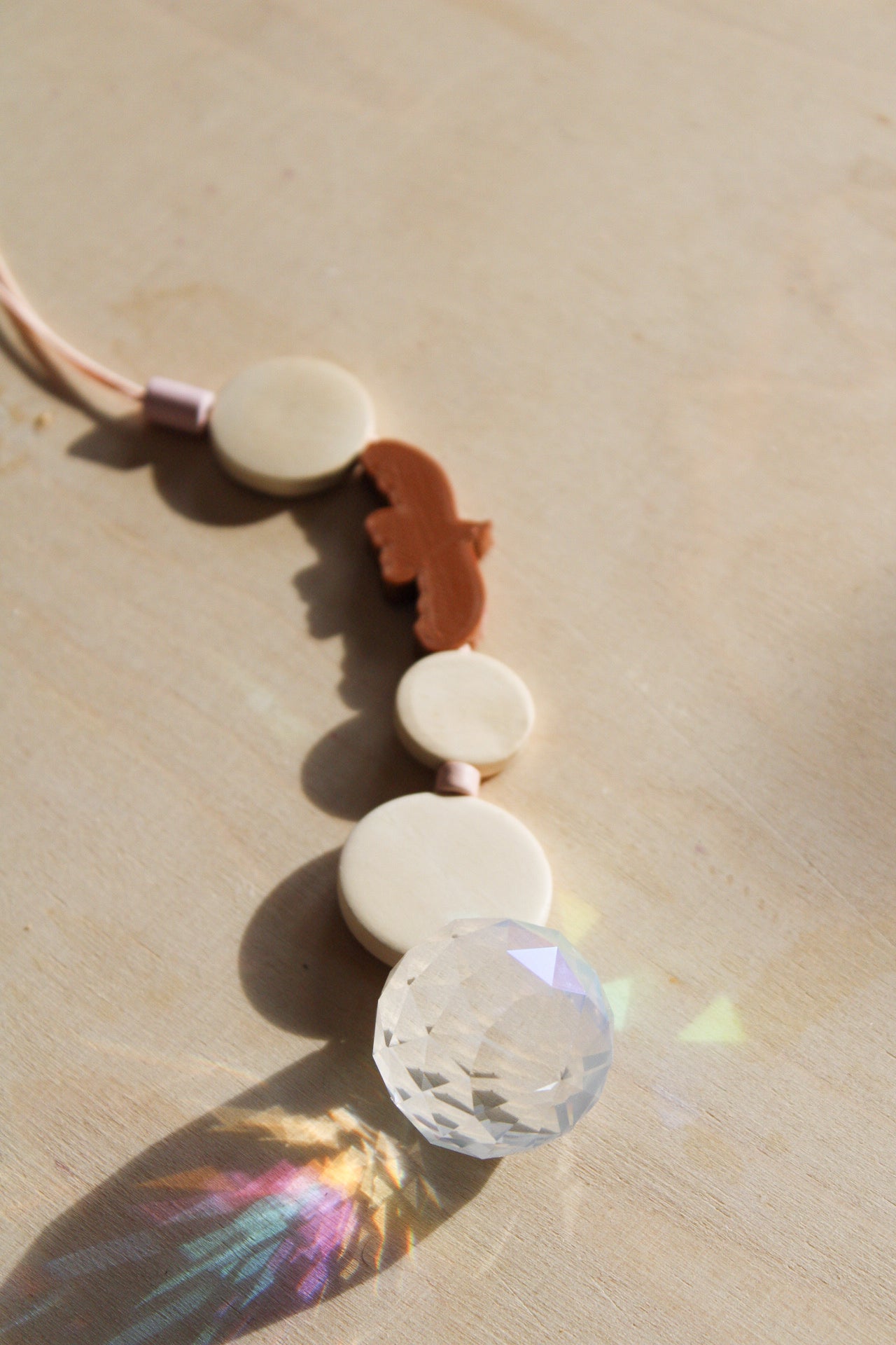 Suncatcher mit einer großen Kristallkugel, Holzperlen, Keramikperlen und 3D-Druck Perle in Form eines Vogels in einem warmen braun fotografiert auf hellem Holz.