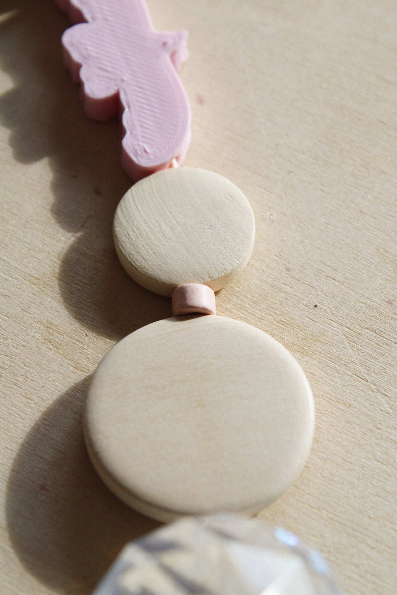 Suncatcher mit einer großen Kristallkugel, Holzperlen, Keramikperlen und 3D-Druck Perle in Form eines Vogels in einem zarten rosa fotografiert auf hellem Holz.